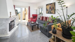 A living room with a fireplace, a red armchair, a grey sofa, and a large painting on the wall.