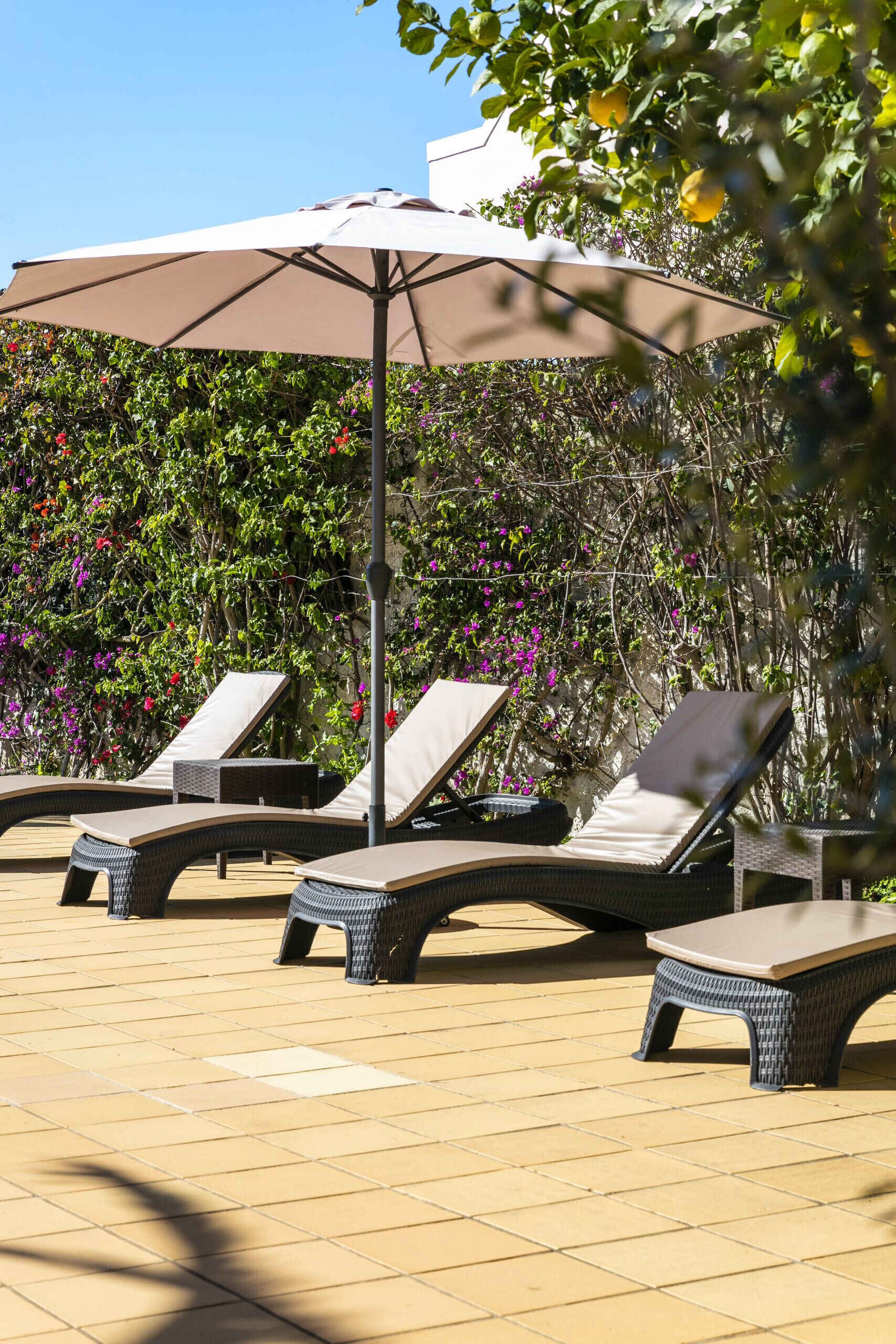 A sunlit outdoor lounge area with wicker lounge chairs and a large umbrella.