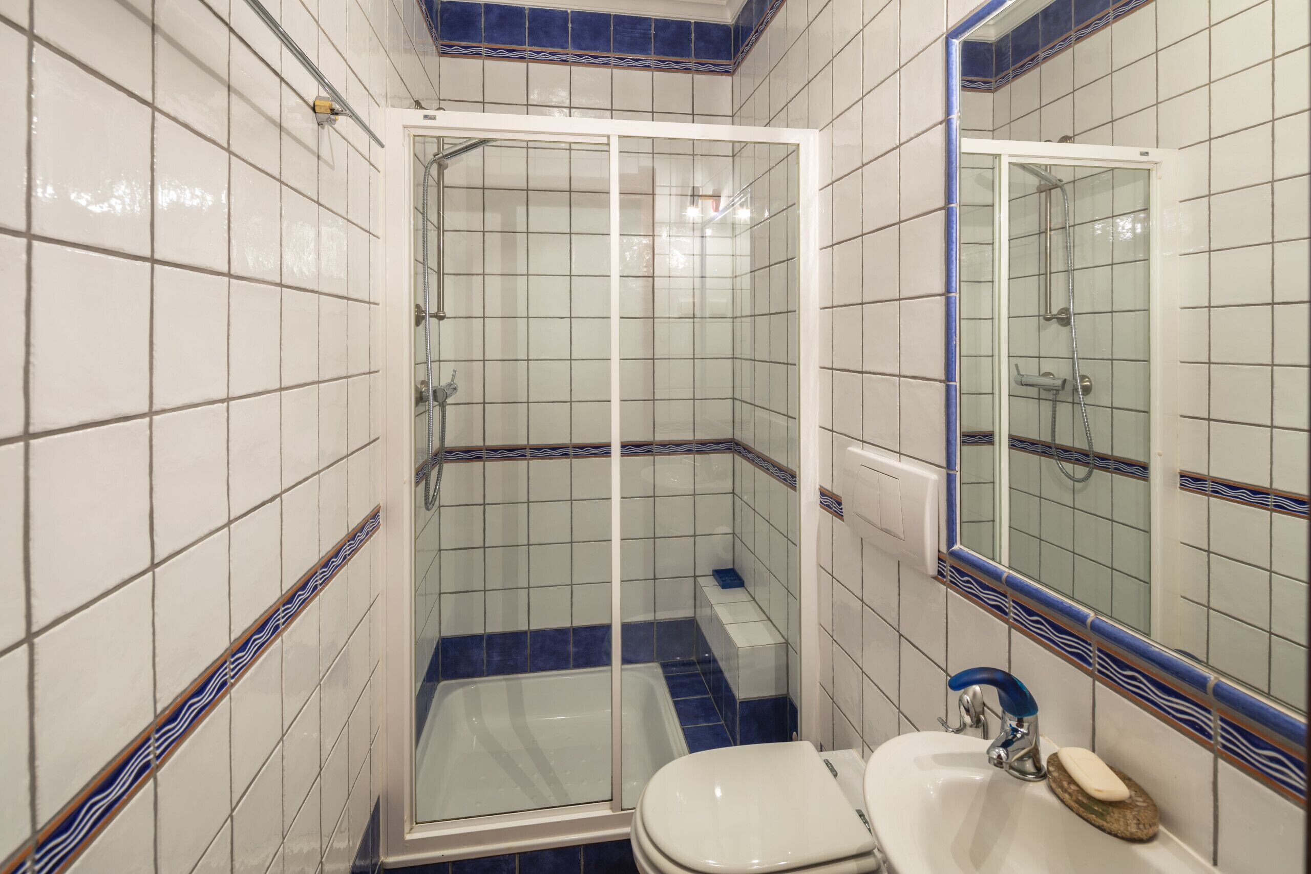 A bathroom with a glass-enclosed shower, a white sink, and a mirror.