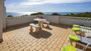 Una terraza con mesa y sillas, vista al mar y una pared blanca con un adorno.