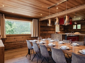 A dining area with a wooden table set for six, a kitchen with red cabinets, and a window overlooking greenery.