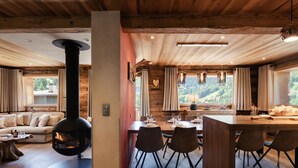 A cozy cabin interior with a fireplace, dining area, and large windows offering a view of the outdoors. - 4★ Chalet, 10 ppl, spa, close to slopes, pets allowed (La Clusaz)