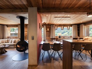 A cozy cabin interior with a fireplace, dining area, and large windows offering a view of the outdoors.
