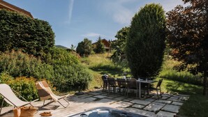 A hot tub with a table and chairs, surrounded by a garden and a hill in the background. - 4★ Chalet, 10 ppl, spa, close to slopes, pets allowed (La Clusaz)