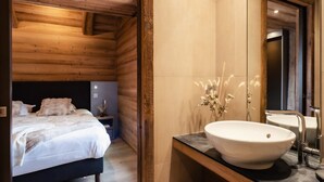 A modern bedroom with a wooden ceiling, a large bed, a nightstand, and a bathroom with a large sink and mirror. - 4★ Chalet, 10 ppl, spa, close to slopes, pets allowed (La Clusaz)