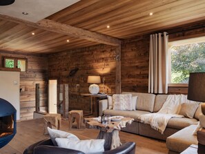 A cozy cabin interior with a wooden ceiling, a sofa, a table, and a fireplace.