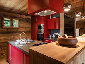 A modern kitchen with red cabinetry, stainless steel appliances, and a wooden island.
