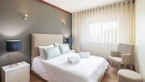 Siististi järjestetty hotellihuone, jossa on sänky, yöpöytälamput, tuoli ja yöpöytä.