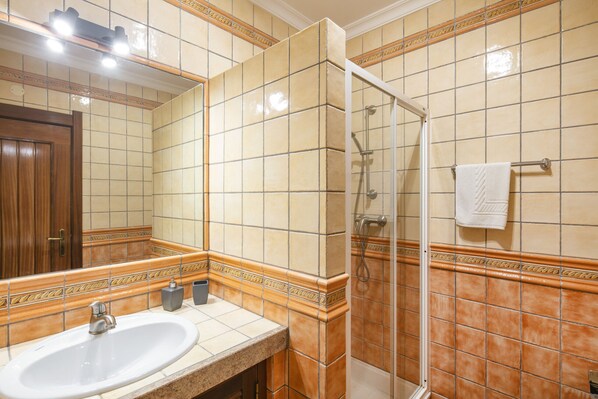 Un baño con lavamanos, espejo, ducha y toallero.
