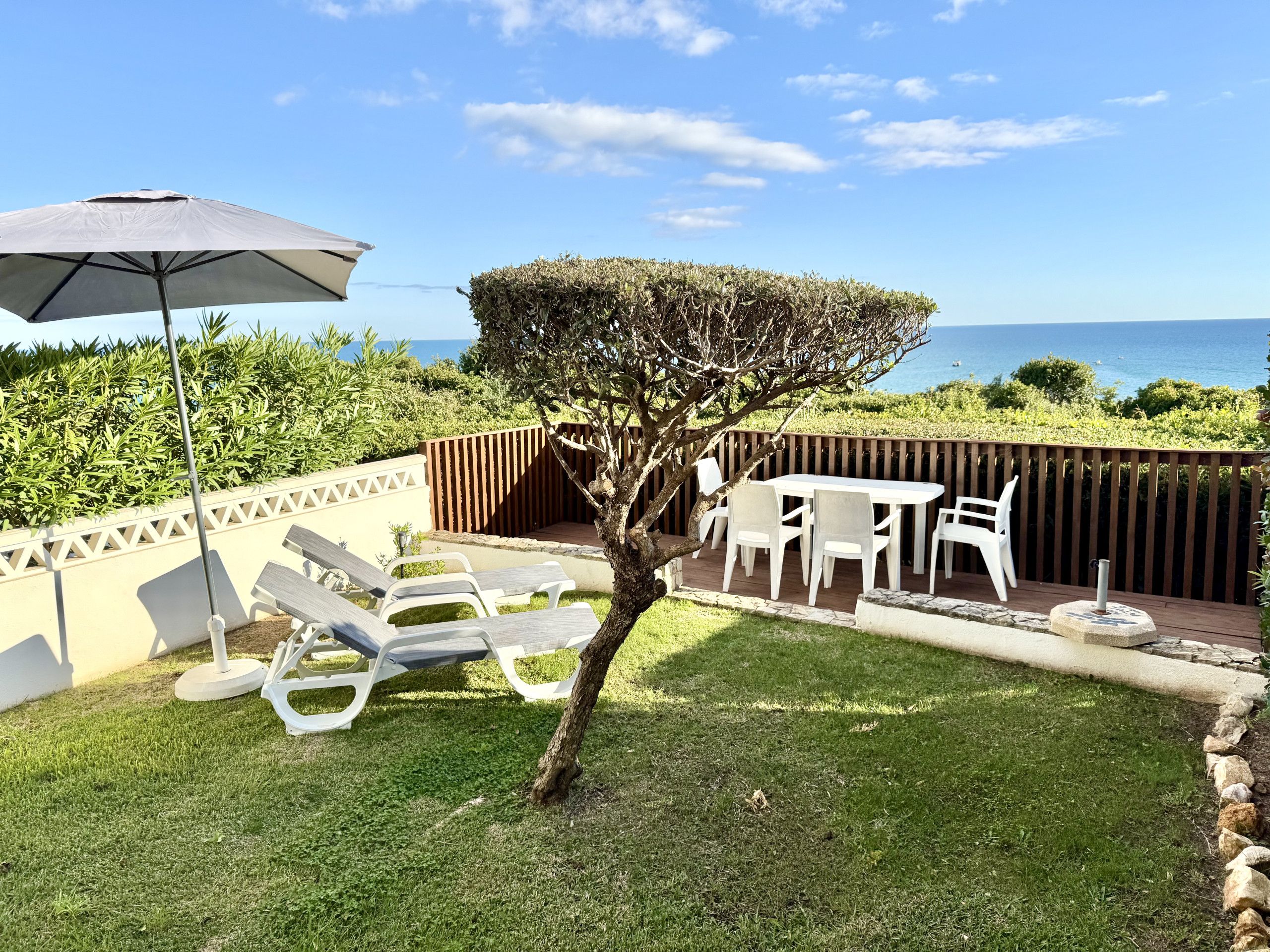 A patio area with a table and chairs, a small tree, and a view of the sea.