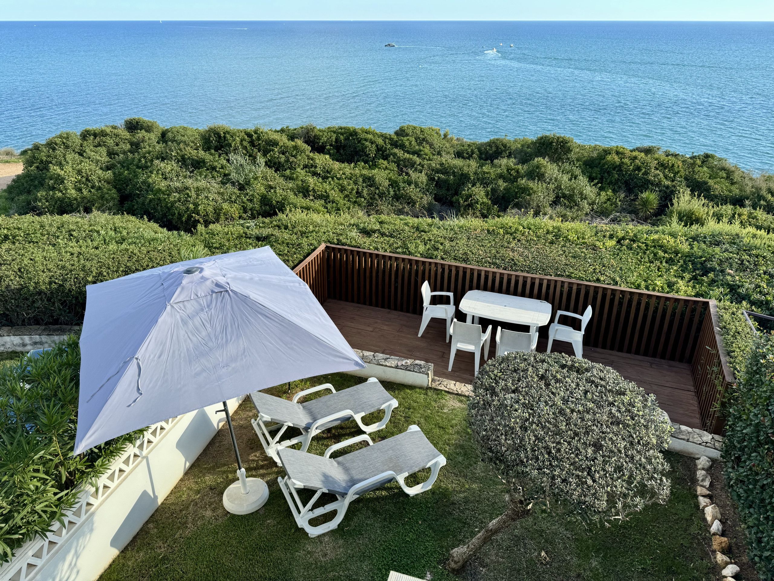 A patio with a table and chairs, a large umbrella, and a view of the sea.