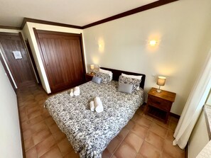 A bedroom with a large bed, two bedside tables, a wooden wardrobe, and a door.