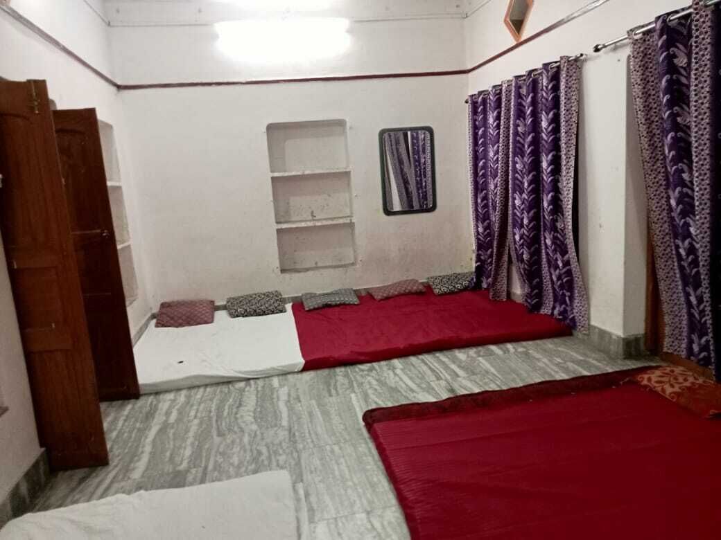 A room with two beds, a small shelf, a mirror, and purple curtains.