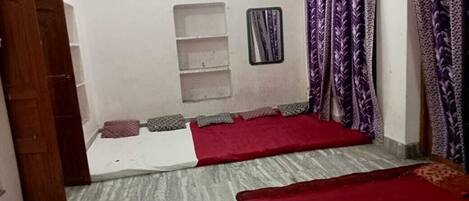 A room with two beds, a small shelf, a mirror, and purple curtains.