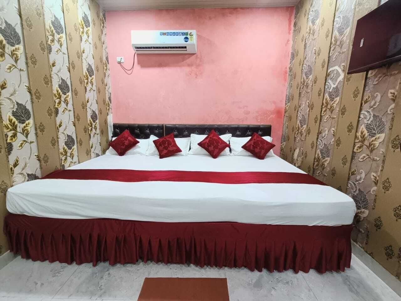 A bed with a red bedspread and matching pillows, a white headboard, and floral wallpaper.