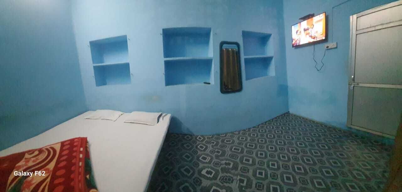 A room with two beds, a TV mounted on the wall, and a patterned floor.