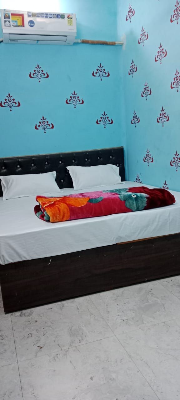 Una cama con sábana blanca y manta colorida, cabecera negra y pared con estampado floral.