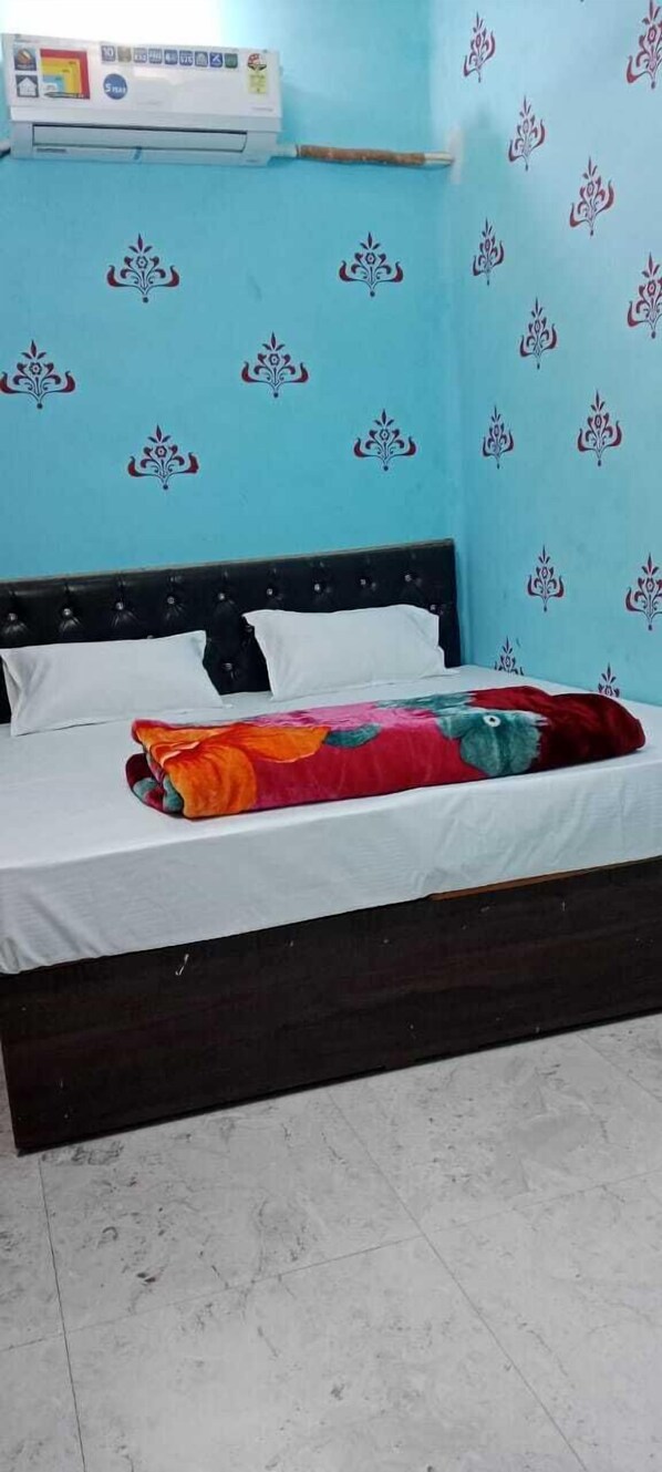Un lit avec un drap blanc et une couverture colorée, une tête de lit noire et un mur orné d’un motif floral.