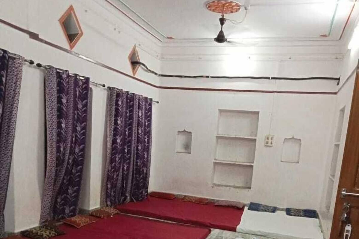 Una habitación con dos camas, un ventilador de techo y una pequeña estantería.