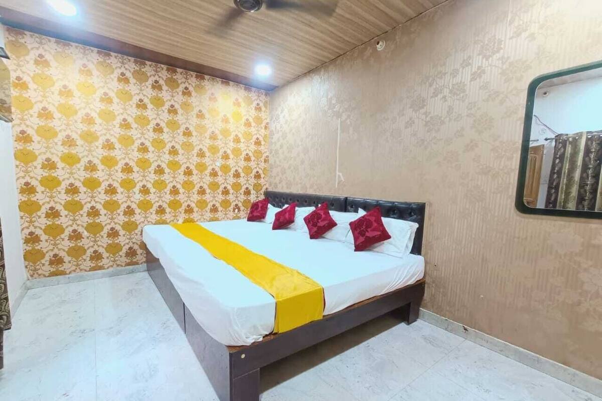 Una cama con detalles en amarillo, almohadas rojas y cabecera en una habitación con papel tapiz estampado y ventilador de techo.