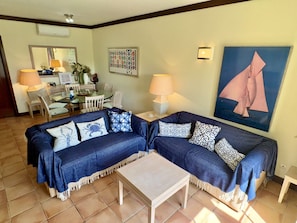 A living room with two blue sofas, a coffee table, and a dining area with chairs and a table. - 21 Terraços de Benagil (Casa Mars) (Benagil)