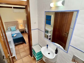 A compact hotel room with a bed, bedside table, and a small bathroom with a sink and mirror.