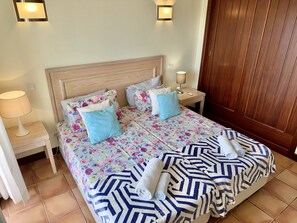 Een net opgemaakt bed met bloemenbeddengoed, twee bedlampjes en een houten deur.