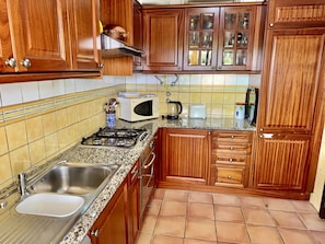 A kitchen with wooden cabinets, a gas stove, a sink, a microwave, and a toaster. - 21 Terraços de Benagil (Casa Mars) (Benagil)