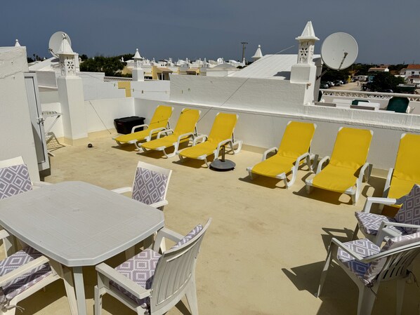 A rooftop terrace with yellow lounge chairs, a white table, and patterned cushions.