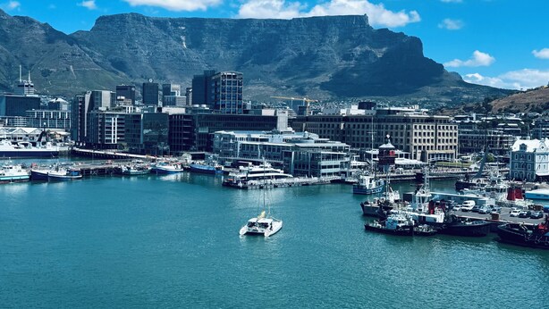 A coastal cityscape with a marina, modern buildings, and a prominent mountain in the background. - Urban Elephant Express The Flamingo (Cape Town)