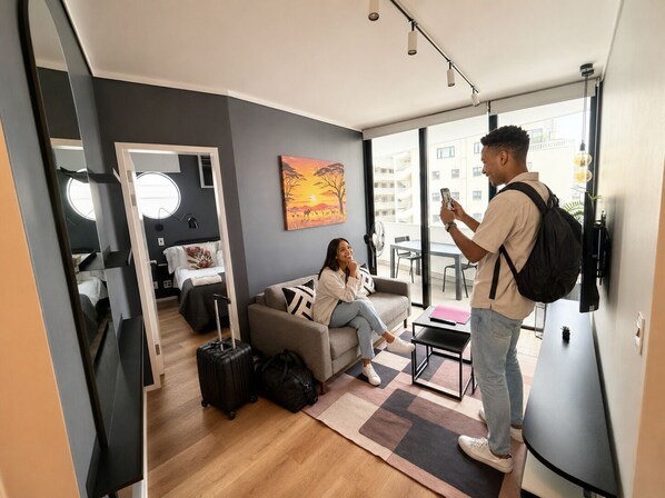 A modern living room with a sofa, a coffee table, and a large window offering a view of the city. - Urban Elephant Express The Flamingo (Cape Town)