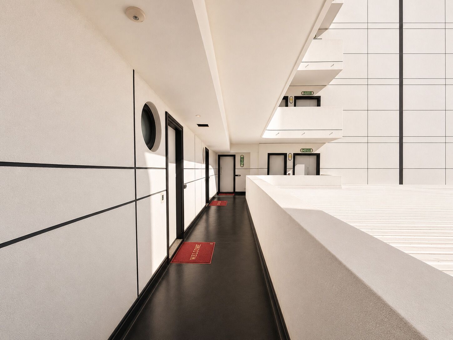 A modern hotel corridor with a reception desk, doors, and a 'WELCOME' mat.