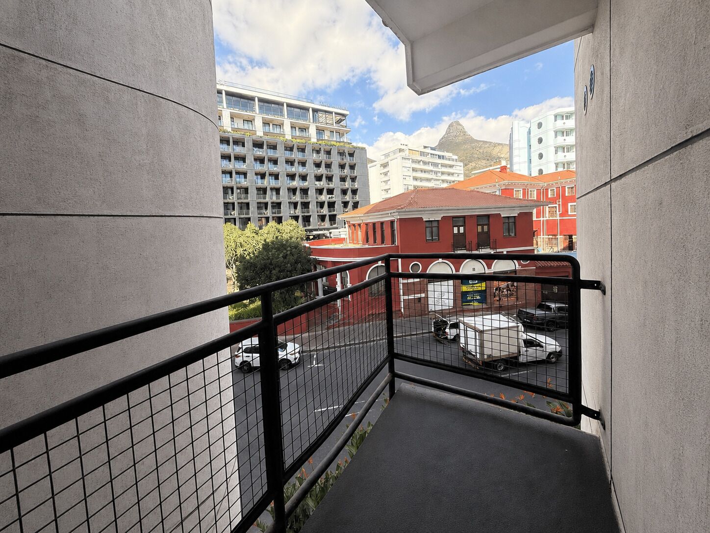 A balcony with a metal railing overlooking a parking area and buildings.