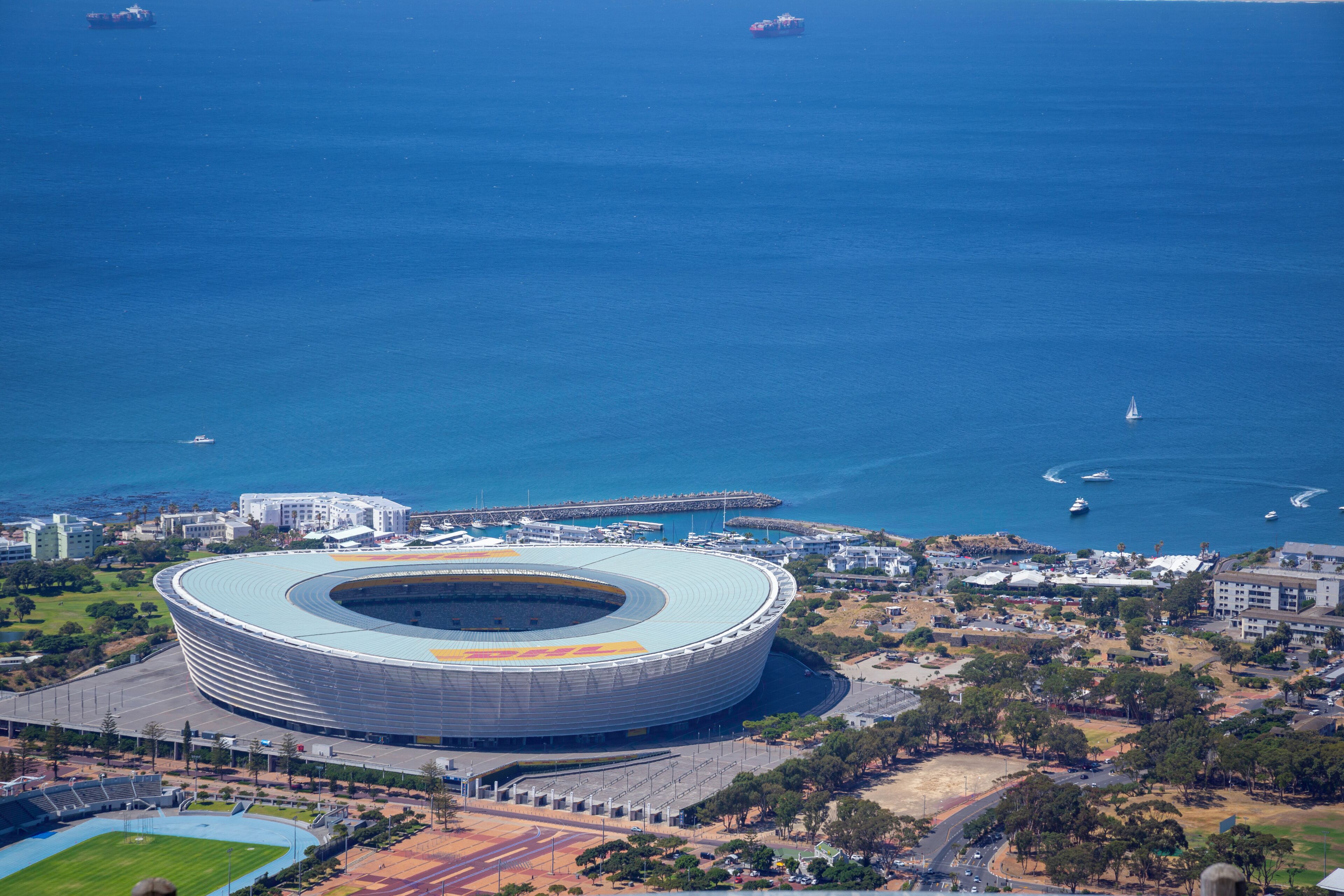 Uno stadio dalla forma circolare, immerso in una zona costiera con barche ed edifici.