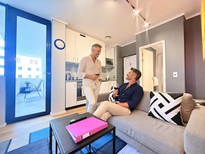 A modern living room with a sofa, a coffee table, and a dining area with a kitchen in the background. - Urban Elephant Express The Flamingo (Cape Town)
