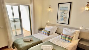 A hotel room with two beds, a sliding glass door to the outside, a framed picture on the wall, and a small bedside table with a lamp.