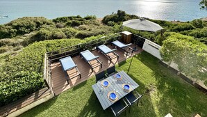 An outdoor patio with a table set for four, surrounded by lush greenery and overlooking a body of water.