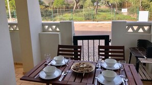 A dining table set for four with white plates, bowls, and cutlery, overlooking a fenced garden with trees. - 45 Terraços de Benagil (Casa Céu Azul) (Benagil)