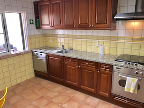 A kitchen with wooden cabinets, a granite countertop, a dishwasher, an oven, and a window with a view. - 45 Terraços de Benagil (Casa Céu Azul) (Benagil)
