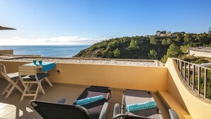 A terrace with two sun loungers, a table with chairs, and a view of the sea and a hill. - Casa Colina Sol 611 - Seaview apartment (Carvoeiro)
