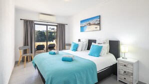 A bedroom with a large bed, a nightstand, a chair, a window with curtains, and a painting on the wall. - Casa Colina Sol 611 - Seaview apartment (Carvoeiro)