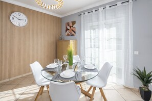 Uma área de jantar com uma mesa redonda de vidro, cadeiras brancas e um relógio na parede.