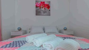 A neatly made bed with pink and blue bedding, two bedside tables with decorative items, and a wall-mounted artwork of red flowers. - Apartman Relax (Crikvenica)