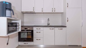 A compact kitchen with white cabinets, a built-in oven, a coffee maker, and a sink. - Apartman Relax (Crikvenica)