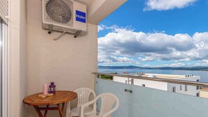 A balcony with a table and chairs, a Haier air conditioner, and a view of the sea and distant mountains. - Apartman Relax (Crikvenica)