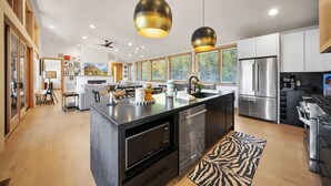 Une cuisine moderne dotée d’un îlot central, d’appareils électroménagers en acier inoxydable et de luminaires suspendus.