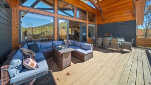 Un espace extérieur aménagé, abrité et doté de mobilier en osier et de tables à plateaux en verre, de grandes fenêtres et d’une vue sur le paysage environnant.