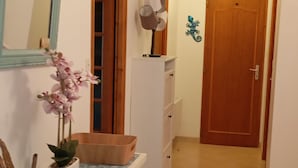A hallway with a white console table, a mirror, a potted plant, a wooden door, and a wall-mounted fan. - Quiet family home 10 minutes walk from the sea (Dolus-d'Oléron)