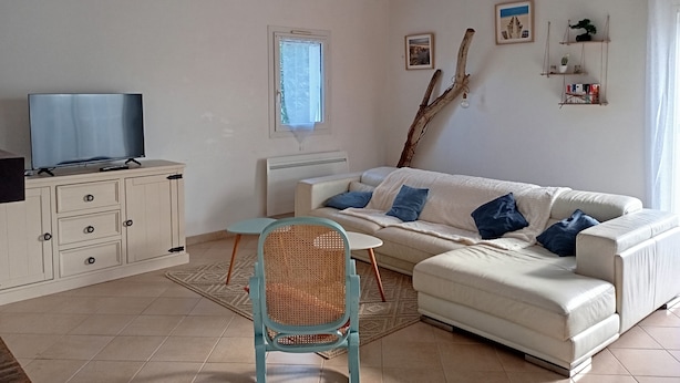 A living room with a sofa, a television, a chair, a window, and a wooden ceiling beam. - Quiet family home 10 minutes walk from the sea (Dolus-d'Oléron)