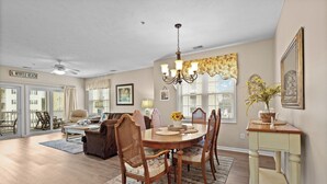 A dining area with a wooden table and chairs, a chandelier, and a view of the outside.